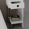 A close-up view of a modern white nightstand with a drawer and a shelf, placed next to a bed. Produktbild-Vorschau