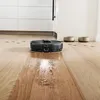 A robot vacuum cleaner is cleaning a wooden floor in a modern kitchen setting. Produktbild-Vorschau