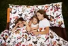 Three children are lying on a bed with a floral and bird-patterned duvet cover outdoors on the grass. Produktbild-Vorschau