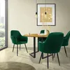 A dining set with four green velvet chairs around a round wooden table, in a room with a large window and a framed picture on the wall. Náhled obrázku produktu