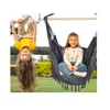 Two young girls are playing outdoors, one hanging upside down from a bar and the other sitting in a hanging chair. Produktbild-Vorschau