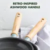Close-up of two frying pan handles with ashwood grips and light blue accents, resting on a white cloth. Náhled obrázku produktu