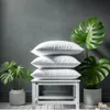 A stack of white pillows on a white stool, flanked by potted plants. Produktbild-Vorschau