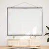 A white projection screen is hanging on a white wall above a wooden cabinet with a plant and a decorative box on top. Náhled obrázku produktu