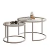 Two nesting coffee tables with glass tops and metal frames, decorated with a candle, a small bowl, and two glasses with a bottle of liquid. Náhled obrázku produktu