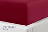 A close-up view of a dark red fitted sheet on a white bed frame. Produktbild-Vorschau