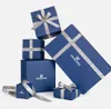 A collection of blue gift boxes with silver ribbon, some stacked and some separate, on a white background. Produktbild-Vorschau