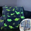 A glow-in-the-dark dinosaur blanket draped over a sofa, with a smaller inset image of the same blanket on a stool. Produktbild-Vorschau