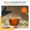 Tea being poured from a kettle into a clear glass cup with a saucer, with some tea leaves and greenery in the background. Produktbild-Vorschau