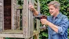 A man is using a cordless drill to assemble a wooden structure, possibly a treehouse or playhouse. Produktbild-Vorschau