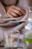 A person's hand rests on a folded blanket with a herringbone pattern, with glasses of drinks in the foreground. Produktbild-Vorschau
