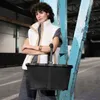 A woman stands with her arms crossed, holding a black mesh basket in front of a blue industrial beam. Voir les images du produit