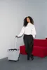 A woman stands next to a shopping trolley in a modern setting with a red sofa in the background. Produktbild-Vorschau