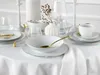 A white table set with white porcelain dishes, gold cutlery, and glasses, suggesting a formal dining setting. Náhľad obrázku produktu
