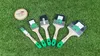 A set of five paintbrushes of varying sizes laid out on a green, grassy surface. A small wooden disc with a logo is also present. Produktbild-Vorschau