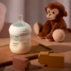 A baby bottle with milk, a stuffed monkey, and wooden toys are arranged on a wooden tray. Podgląd zdjęcia produktu