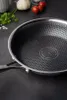A close-up view of a frying pan with a honeycomb pattern on its surface, placed on a dark, textured surface. In the background, there are some cherry tomatoes, garlic, and parsley. Náhľad obrázku produktu
