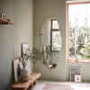 A modern living room with a unique, frameless mirror on the wall, reflecting a window and plants. A wooden bench with vases and artwork is placed below the mirror. Produktbild-Vorschau