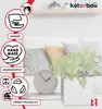 A white ceramic planter with a geometric pattern sits on a shelf next to a clock and pillows, with a plant inside. Produktbild-Vorschau