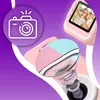 A close-up marketing image of a pink children's camera with a screen displaying a photo of happy children. The camera's lens is prominently featured, with a graphic overlay of a camera icon with a flash. Anteprima dell’immagine prodotto