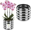 A pink orchid plant in a silver pot sits next to a stack of silver rings. Produktbild-Vorschau