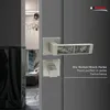 A close-up of a modern door handle set with a decorative inlay, mounted on a gray door. The background shows a glimpse of an interior with marble-like columns and furniture. Produktbild-Vorschau