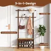 A wooden coat rack with a shoe bench and shoe shelves, set against a white door and wall, with a potted plant to the side. Produktbild-Vorschau
