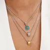 A close-up shot of a person wearing three layered silver necklaces with different charms. Podgląd zdjęcia produktu