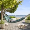 A hammock is set up on a wooden deck overlooking a body of water with boats in the distance. Produktbild-Vorschau