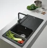 A modern black granite kitchen sink with a faucet and a cutting board, along with some vegetables and a pot in the background. Produktbild-Vorschau