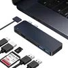 A dark gray USB-C hub is shown connected to a laptop, with various cables and memory cards scattered around it. Produktbild-Vorschau