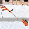 A person is using an electric snow blower on a snowy surface in front of a wooden building. Podgląd zdjęcia produktu