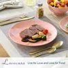 A table setting with a pink marble-patterned plate of food, cutlery, and a fruit bowl. Produktbild-Vorschau