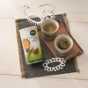 A can of Naturata Getreidekaffee Zimt und Kardamom with two cups of coffee on a tray, set on a textured mat. Náhľad obrázku produktu