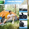 A man is sitting in front of a tent in a forest, holding a phone. The image highlights the charging methods of a solar radio. Produktbild-Vorschau
