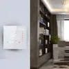 A smart thermostat is mounted on a textured wall next to a bookshelf filled with books and plants. A desk with a laptop is visible in the background. Podgląd zdjęcia produktu