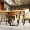 A modern dining room with a wooden table and chairs, featuring a prominent metal table leg. Voir les images du produit