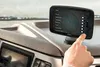 A hand is shown interacting with a GPS navigation device mounted on a vehicle's dashboard. Voir les images du produit