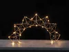 A geometric star-shaped light decoration with warm white LED lights, set against a dark background and resting on a light gray surface. Produktbild-Vorschau