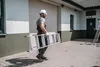 A construction worker carrying a ladder outside a building. Anteprima dell’immagine prodotto
