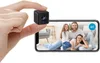 A hand holds a mini camera over a smartphone displaying a family video. Produktbild-Vorschau
