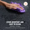 A hand is wiping a black speckled surface with a purple cloth, with water spills on the surface. Voir les images du produit
