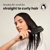 A woman is brushing her wet hair with a black hairbrush. The background is a plain, light color. Produktbild-Vorschau