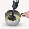 A hand is holding a pot while an immersion blender is being used to blend food inside the pot. Produktbild-Vorschau