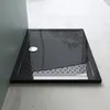 A black rectangular shower tray with a textured surface and a silver drain cover, placed on a light gray floor next to a dark gray wall. Produktbild-Vorschau