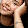 A close-up shot of a young woman's face and arm, wearing a Pandora bracelet with a crown charm. Produktbild-Vorschau