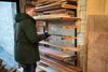A man is selecting a piece of wood from a storage rack in a workshop. Náhled obrázku produktu