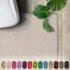 A shaggy cream-colored rug is shown with a white sofa and a monstera plant on a wooden floor. Below the rug, there are swatches of different colored rugs. Produktbild-Vorschau
