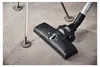 A close-up shot of a vacuum cleaner head on a wooden floor, with parts of furniture legs visible in the background. Produktbild-Vorschau