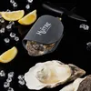 An oyster knife with a silicone holder, lemons, ice cubes, and an open oyster on a black reflective surface. Produktbild-Vorschau